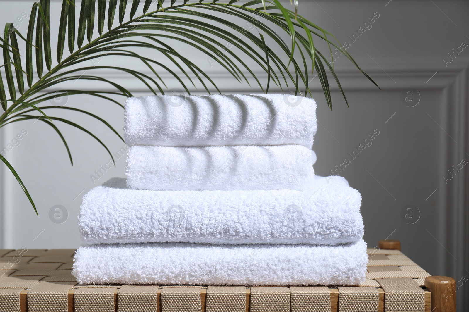 Photo of Stacked terry towels and green leaf on wicker bench indoors