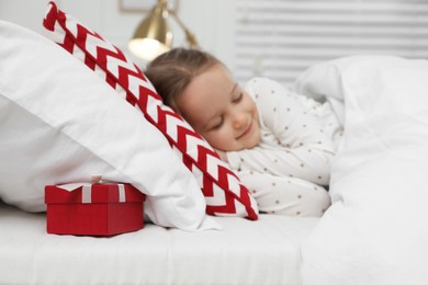 Photo of Cute little girl sleeping in bed, gift box under pillow. Saint Nicholas day tradition