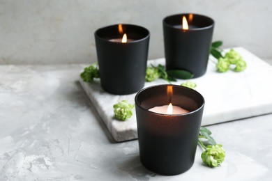 Photo of Burning candles with flowers on grey table, space for text