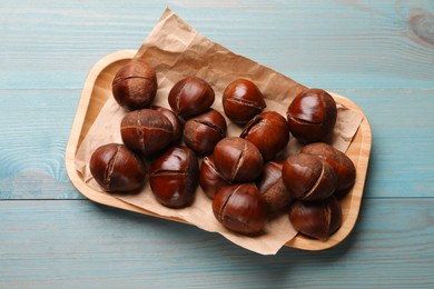 Photo of Fresh edible sweet chestnuts in serving plate on light blue wooden table, top view