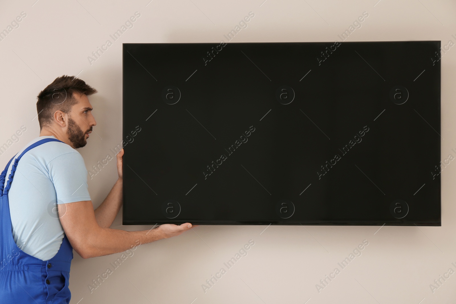 Photo of Professional technician installing modern flat screen TV on wall indoors