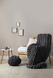 Photo of Soft chunky knit blanket on armchair in room. Interior design