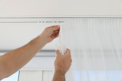 Worker hanging window curtain indoors, low angle view