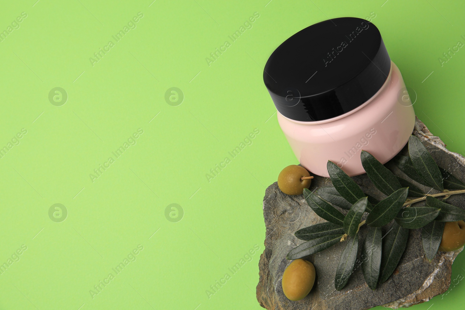 Photo of Jar of cream and olives on light green background, flat lay. Space for text