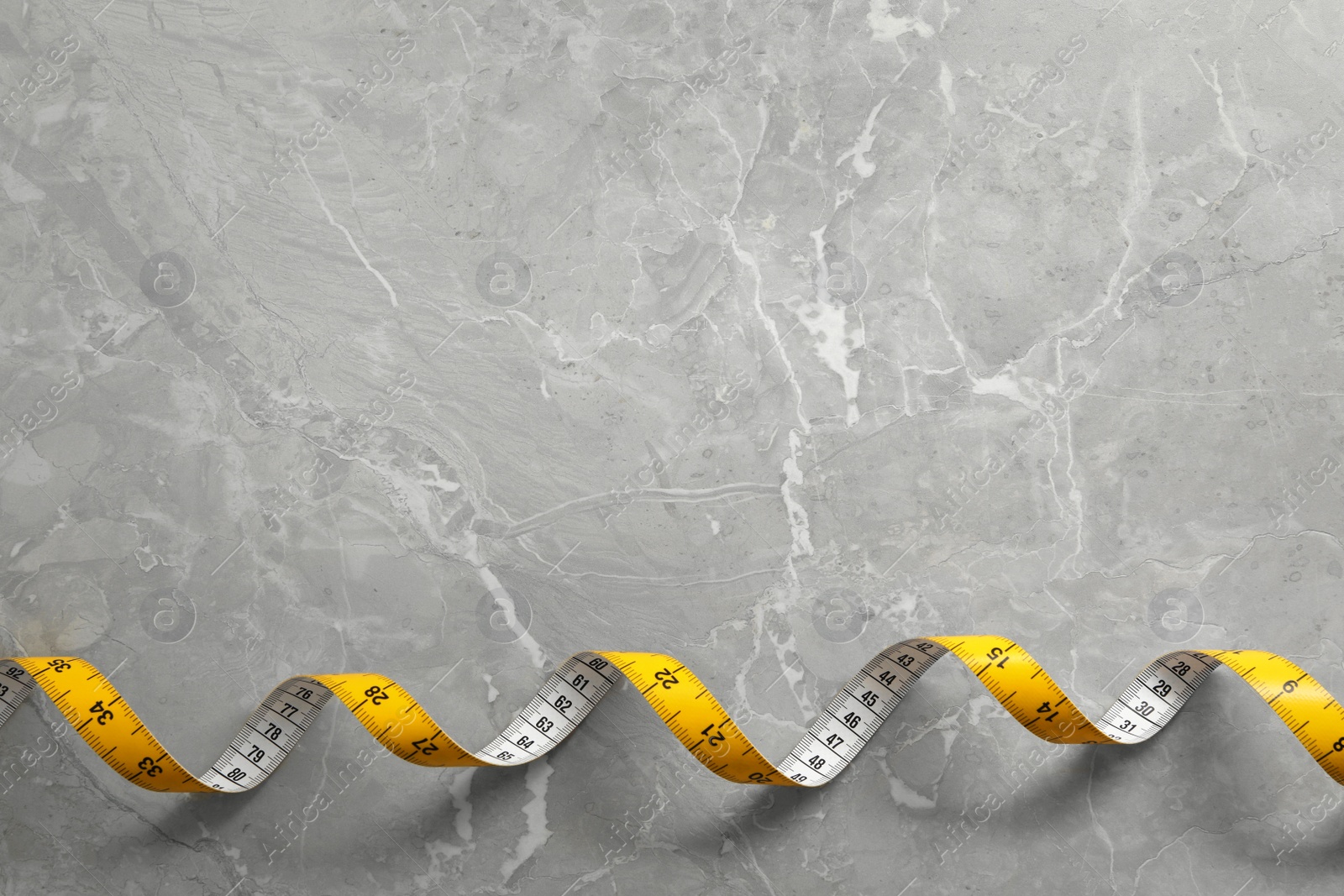 Photo of Measuring tape on light grey marble table, top view. Space for text