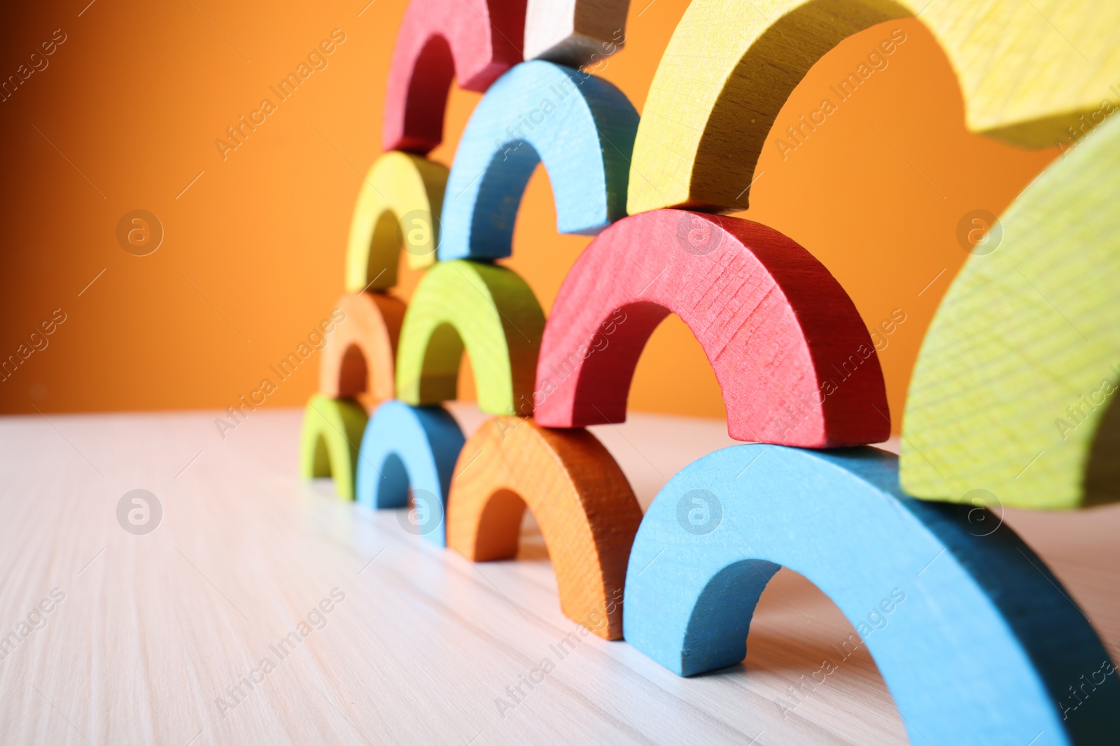 Photo of Colorful wooden pieces of educational toy on light table against orange wall, closeup and space for text. Motor skills development