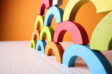 Photo of Colorful wooden pieces of educational toy on light table against orange wall, closeup and space for text. Motor skills development