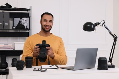 Photo of Young professional photographer with camera at table in modern photo studio