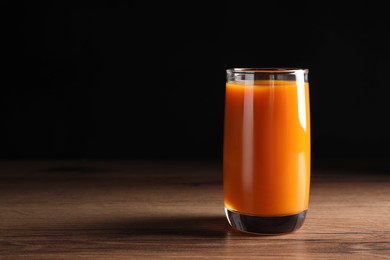 Glass of tasty carrot juice on wooden table against black background, space for text