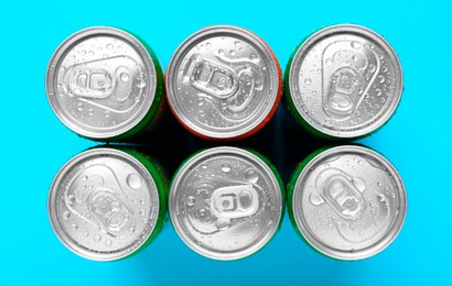 Photo of Energy drinks in wet cans on light blue background, top view