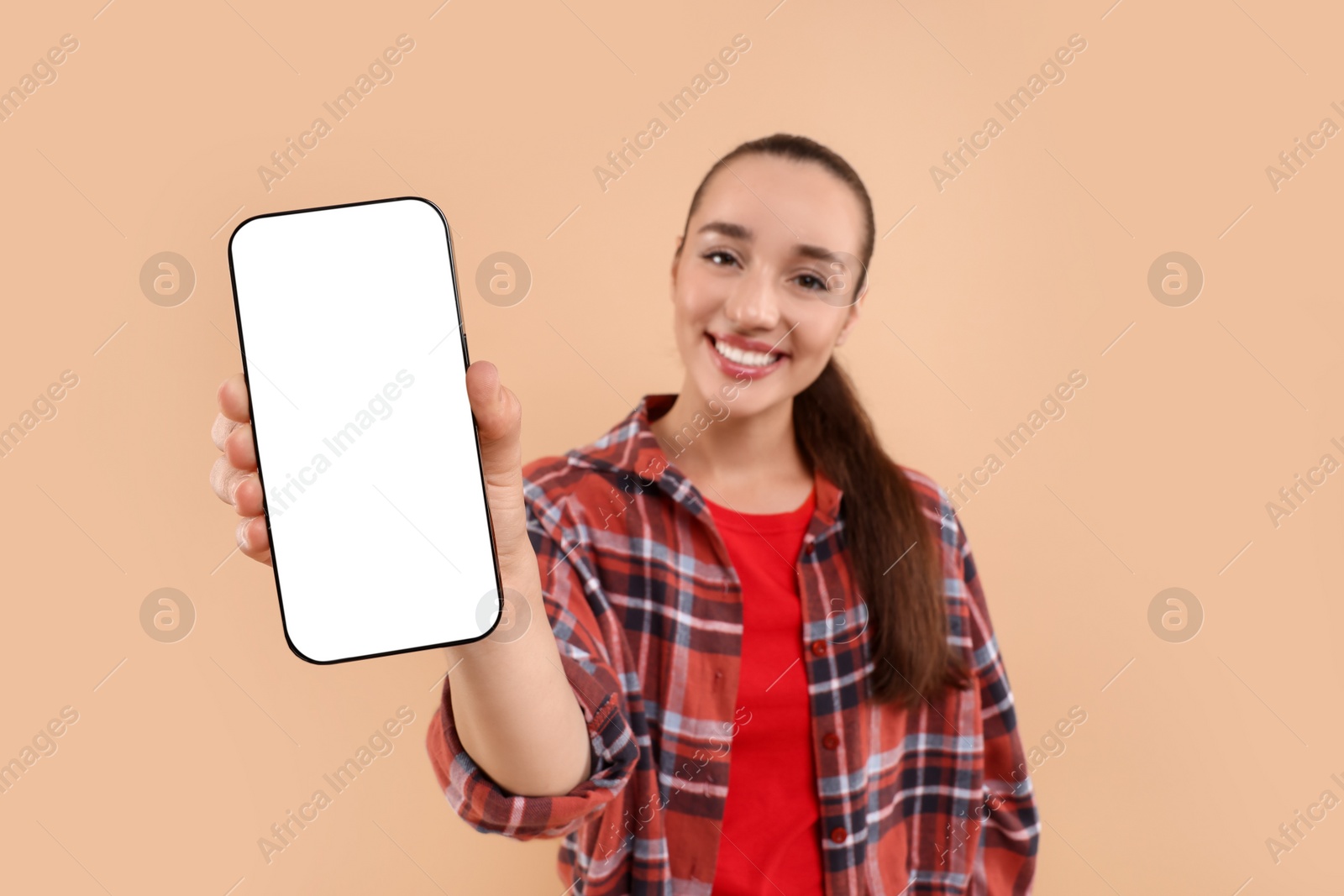 Photo of Young woman showing smartphone in hand on light brown background, selective focus. Mockup for design