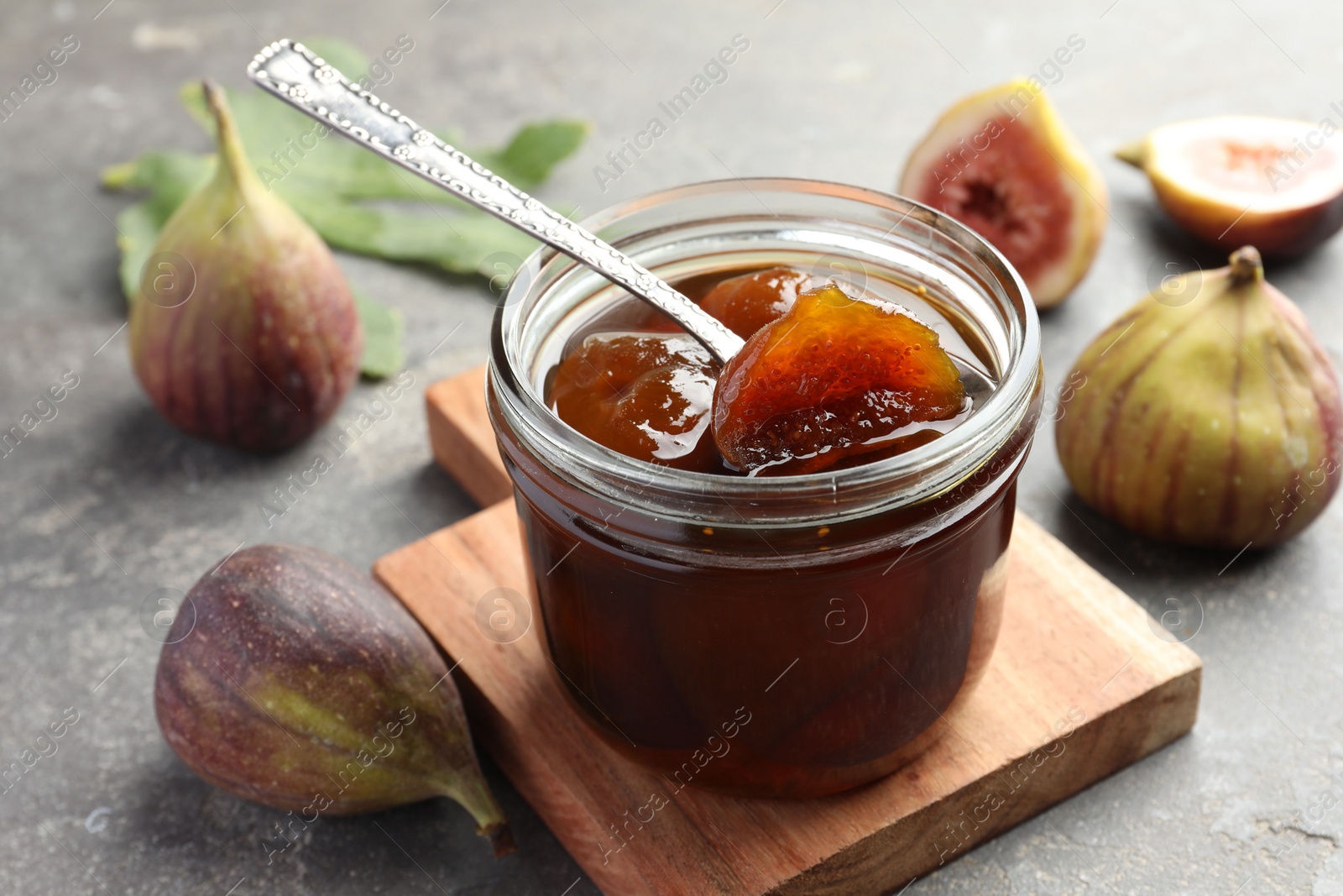 Photo of Jar of tasty sweet jam and fresh figs on grey table