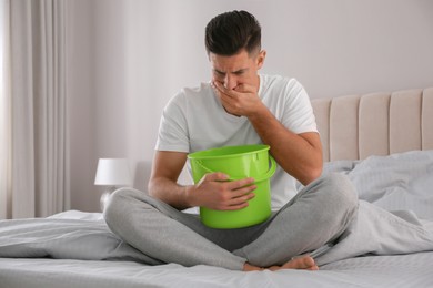 Photo of Man with bucket suffering from nausea on bed at home. Food poisoning