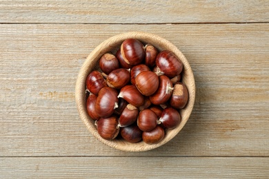 Photo of Fresh sweet edible chestnuts in bowl on wooden table, top view
