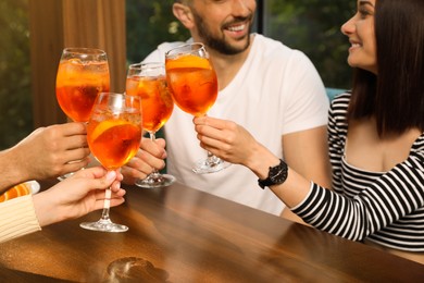 Friends clinking glasses of Aperol spritz cocktails at table, closeup