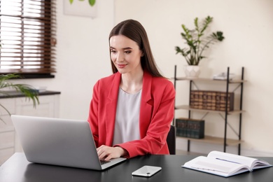 Photo of Young businesswoman using laptop at table in office