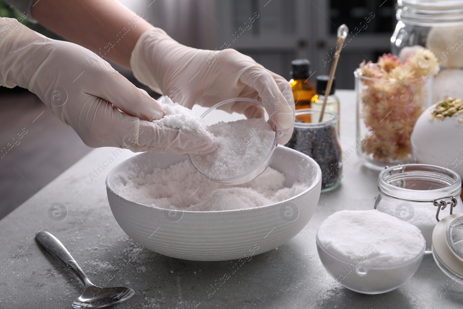 Photo of Woman in gloves making bath bomb at grey table, closeup