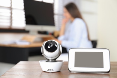 Photo of Baby monitor and camera on table and woman working in home office. Video nanny