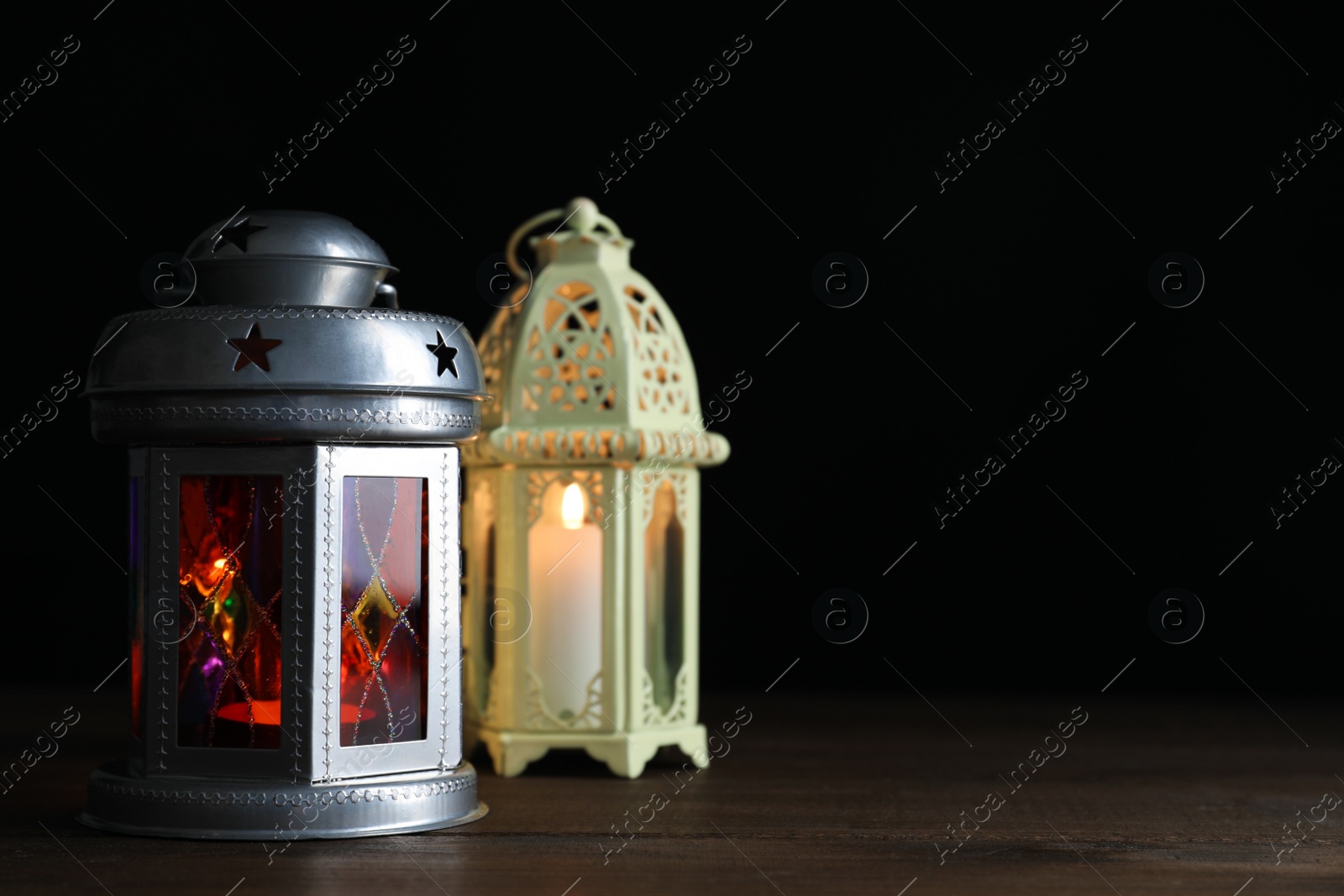Photo of Decorative Arabic lanterns on wooden table against black background, space for text