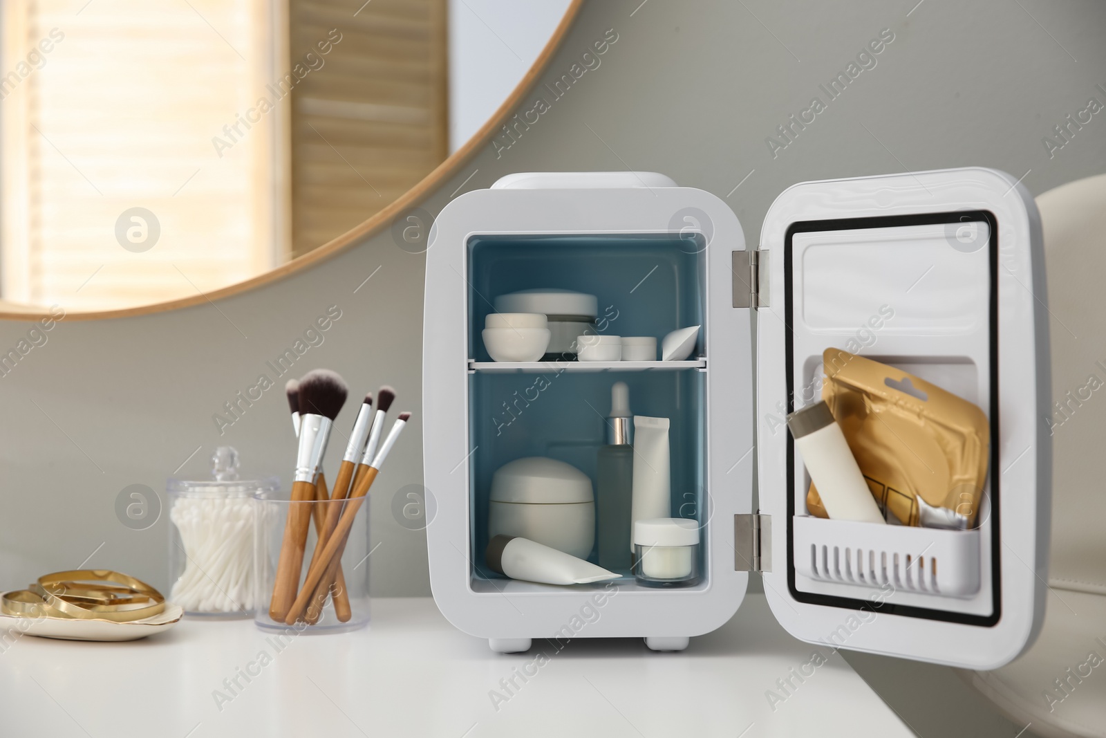 Photo of Cosmetics refrigerator and skin care products on white vanity table indoors