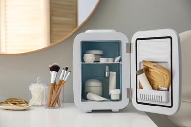 Photo of Cosmetics refrigerator and skin care products on white vanity table indoors