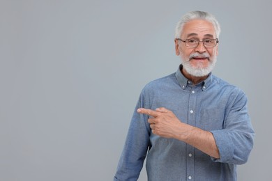 Photo of Special promotion. Smiling senior man pointing at something on light grey background. Space for text