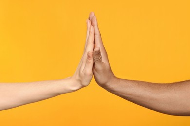 Photo of International relationships. People giving high five on orange background, closeup