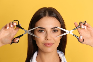 Young hairstylist holding professional scissors on color background