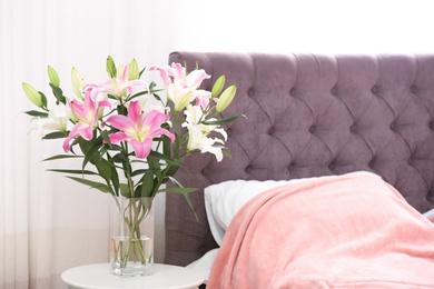 Vase with bouquet of beautiful lilies on table in bedroom. Space for text