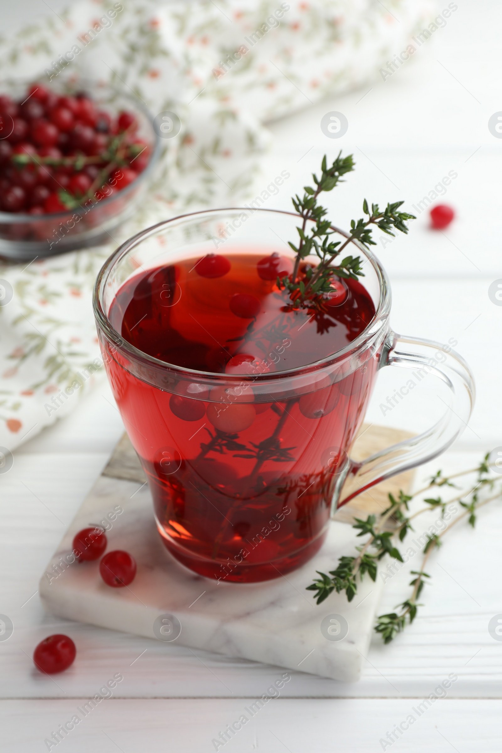 Photo of Tasty hot cranberry tea with thyme and fresh berries in glass cup on white wooden table