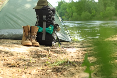 Modern camping tent and equipment on riverbank. Space for text