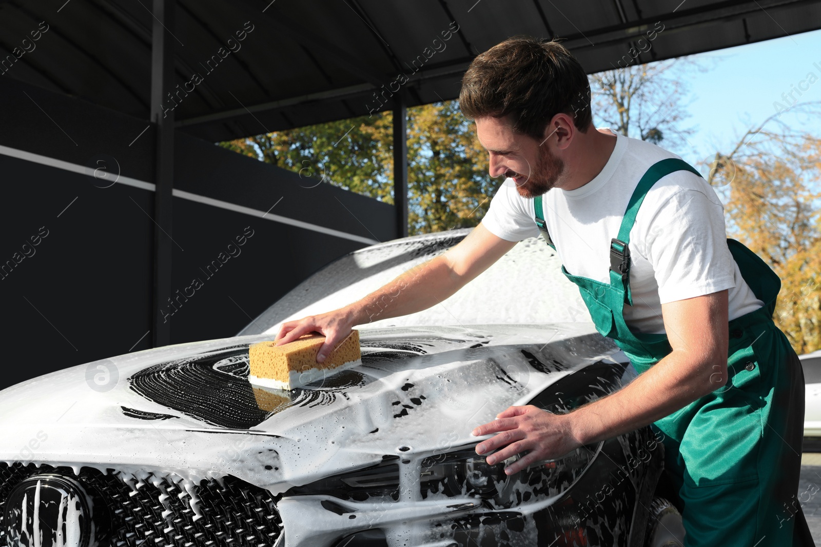 Photo of Worker washing auto with sponge at outdoor car wash