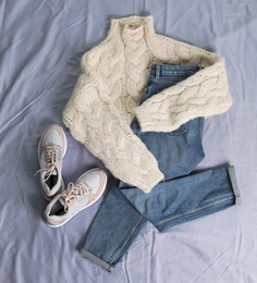 Flat lay composition with jeans, sweater and shoes on color fabric