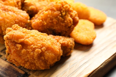Tasty deep fried chicken pieces and nuggets on serving board, closeup