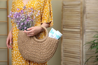 Photo of Woman holding beach bag with beautiful bouquet of wildflowers and magazine indoors, closeup. Space for text