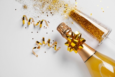 Bottle of champagne and glass with gold glitter on white background, top view. Hilarious celebration