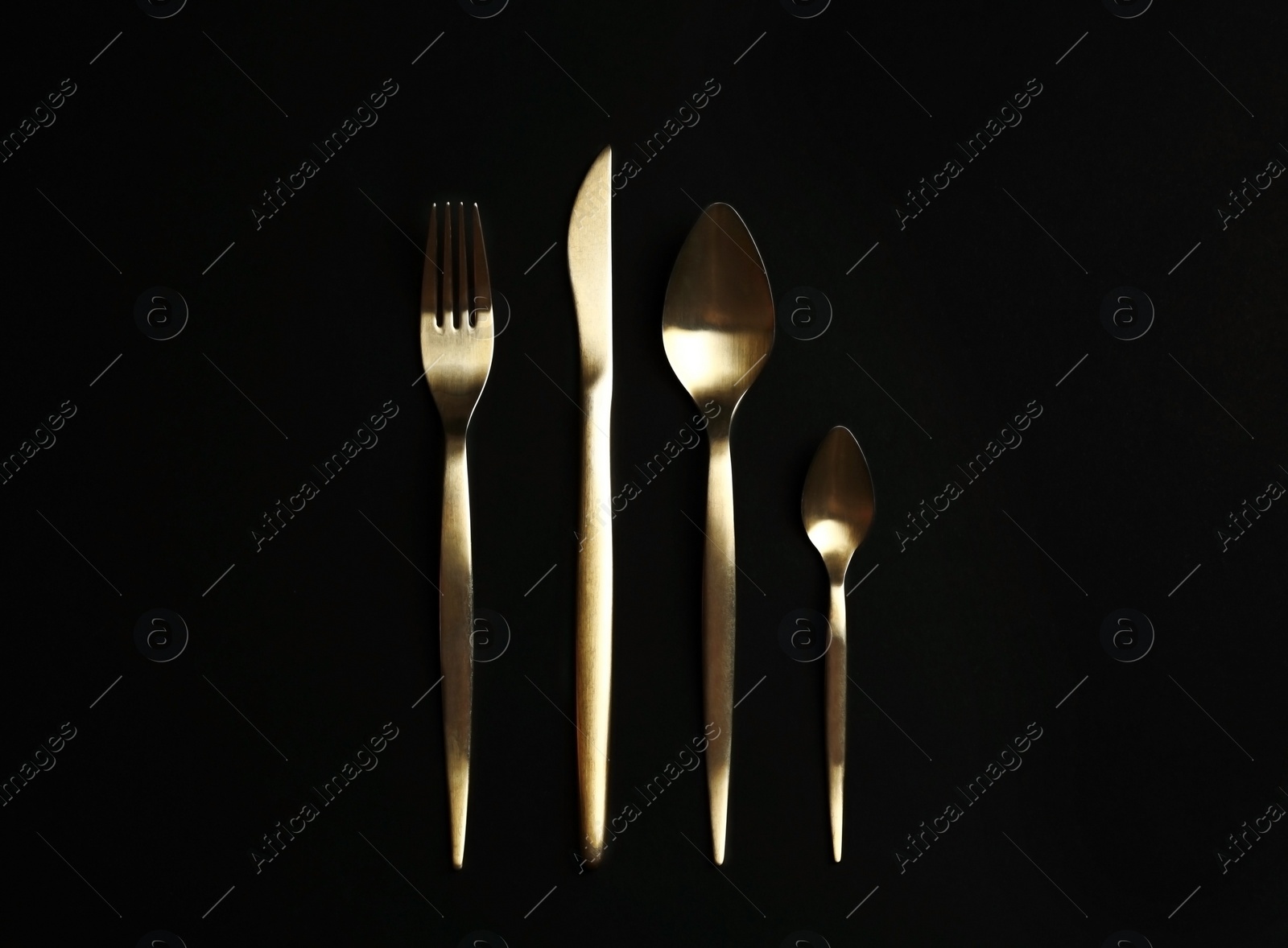 Photo of Set of gold cutlery on black background, flat lay