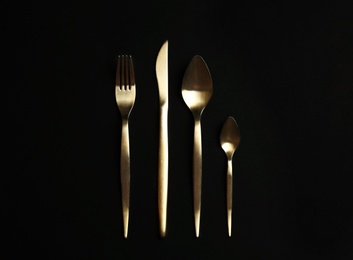 Photo of Set of gold cutlery on black background, flat lay