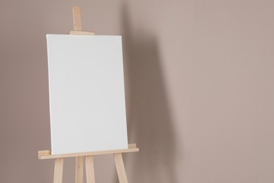 Photo of Wooden easel with blank canvas on beige background. Space for text