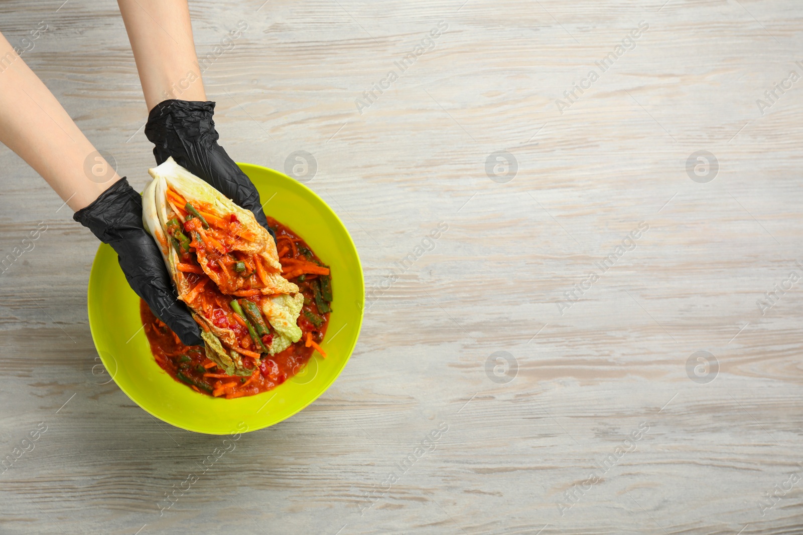 Photo of Woman preparing spicy cabbage kimchi at wooden table, top view. Space for text