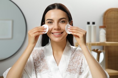 Photo of Young woman using cotton pads with micellar water indoors