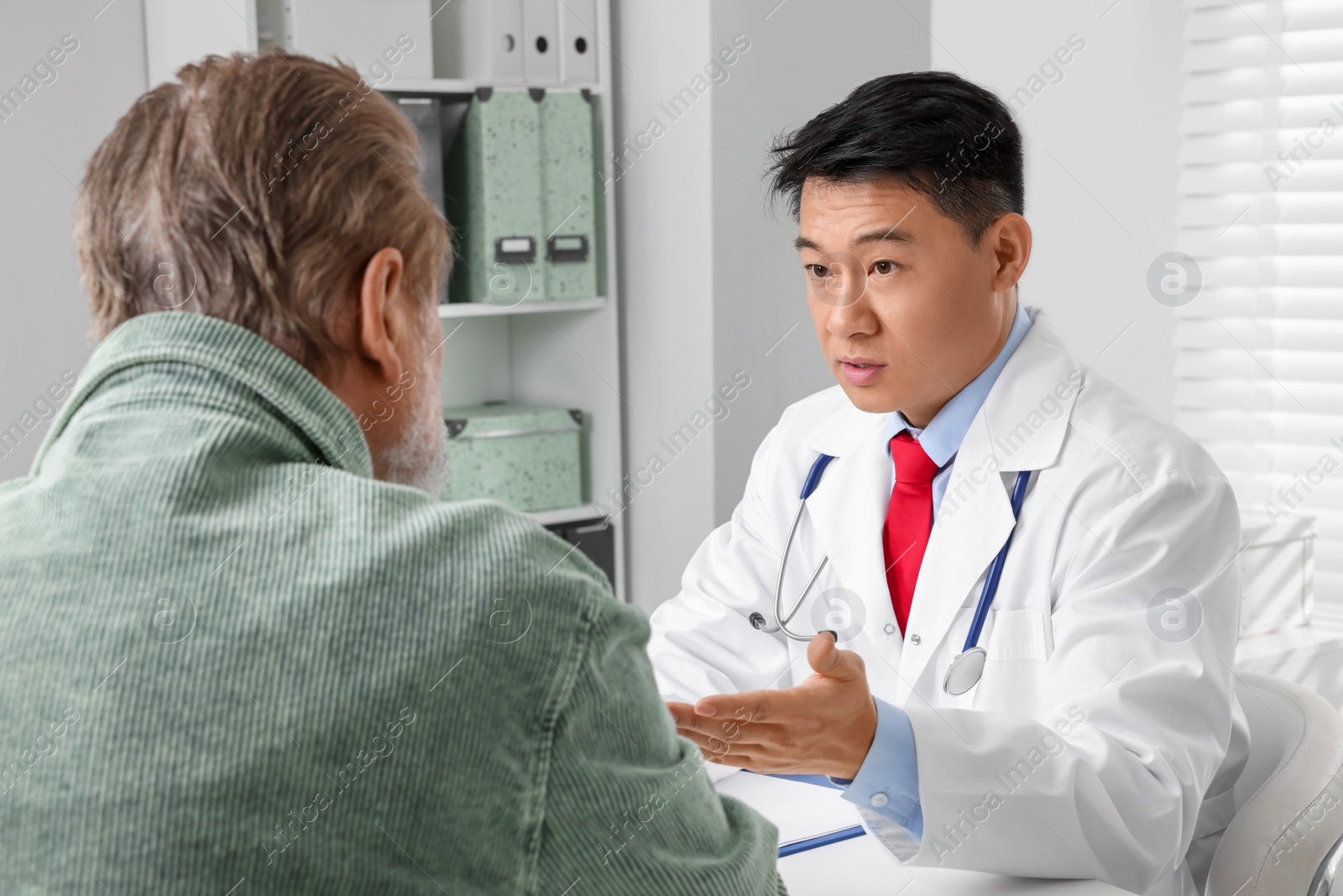 Photo of Doctor consulting senior patient at white table in clinic