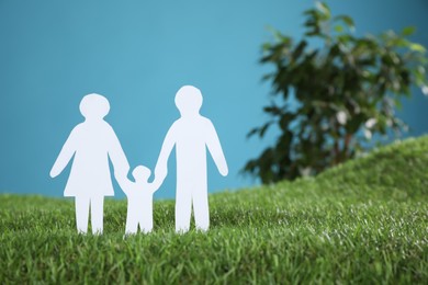 Photo of Paper cutout of parents with their child on green grass against light blue background, space for text. Family Day
