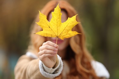 Woman showing autumn leaf outdoors, selective focus