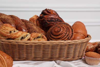 Wicker basket with different tasty freshly baked pastries on table, closeup