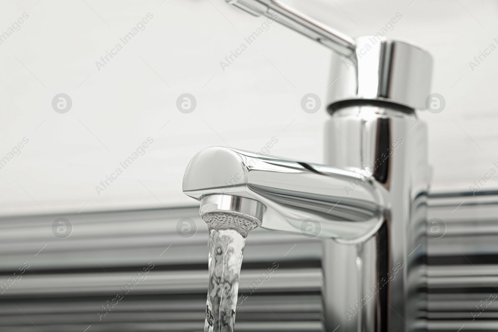 Photo of Water flowing from tap on blurred background, closeup. Space for text