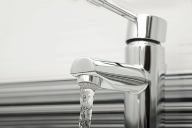 Photo of Water flowing from tap on blurred background, closeup. Space for text