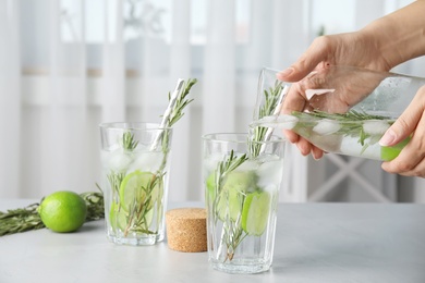 Photo of Woman pouring lime cocktail into glass with rosemary on table, closeup