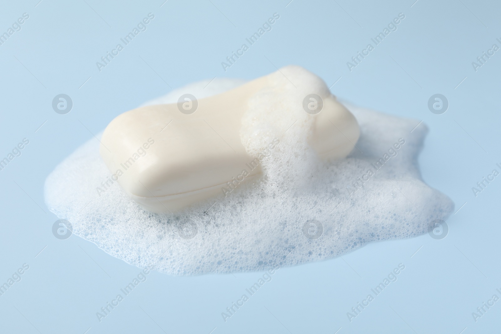 Photo of Soap with fluffy foam on light blue background