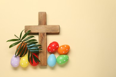 Wooden cross, painted Easter eggs and palm leaf on beige background, flat lay. Space for text
